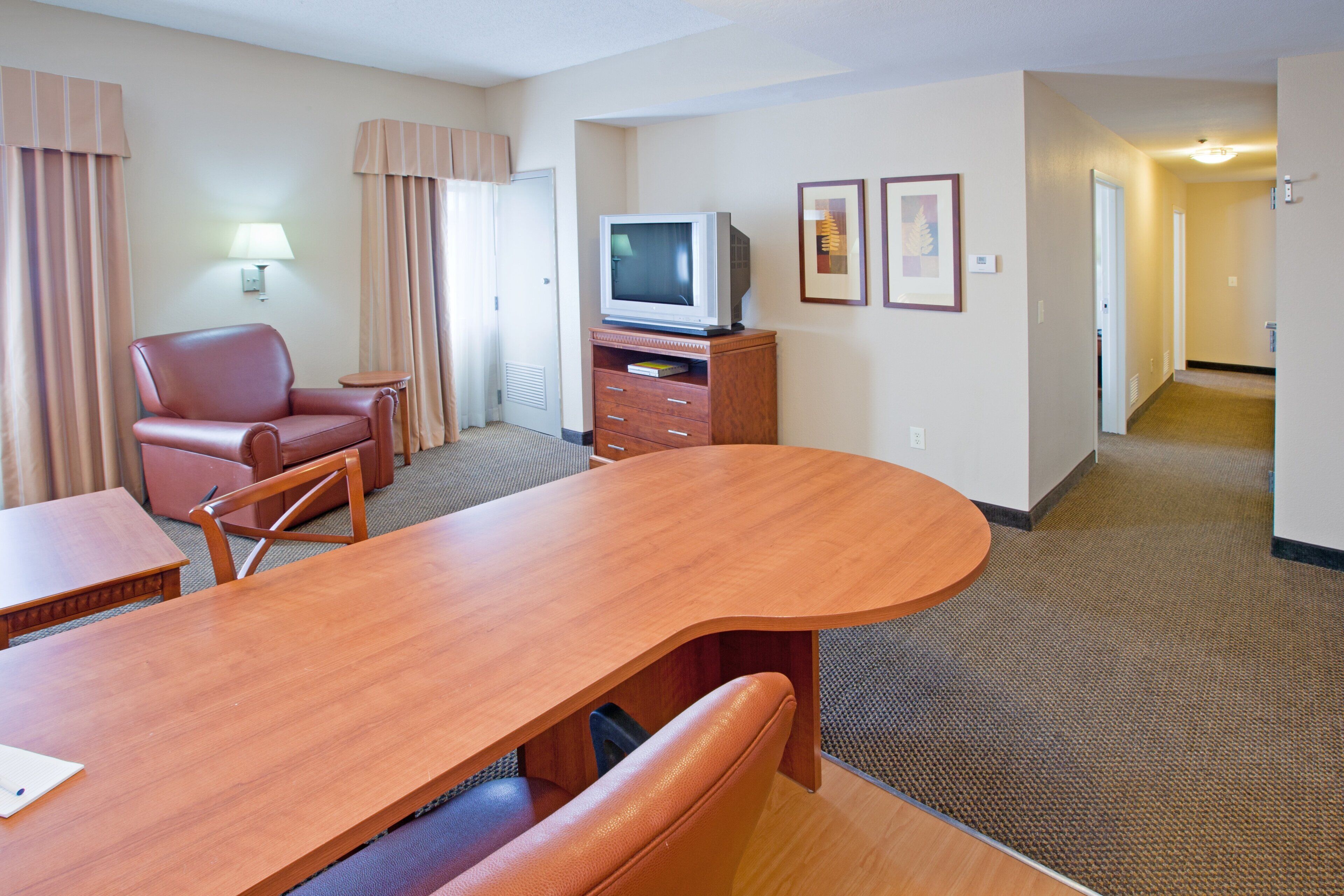 A hotel room with a wooden dining table, a leather chair, a television, and a small cabinet.
