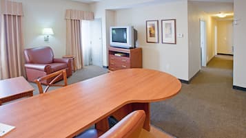 A hotel room with a wooden dining table, a leather chair, a television, and a small cabinet.