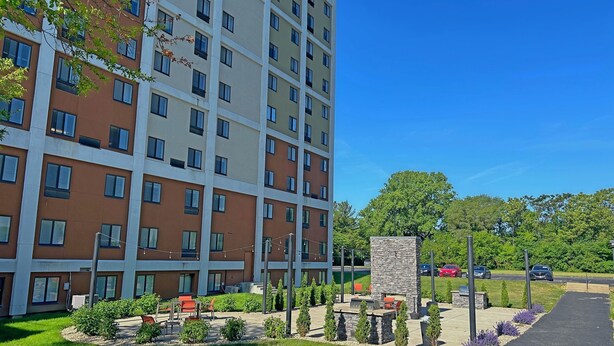 Un edificio residencial de varios pisos con un patio ajardinado que cuenta con mobiliario exterior y una chimenea de piedra.
