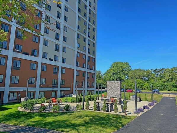 Un edificio residencial de varios pisos con un patio ajardinado que cuenta con mobiliario exterior y una chimenea de piedra.