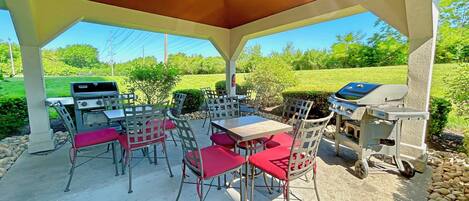An outdoor patio with a covered seating area, a grill, and a table with chairs.
