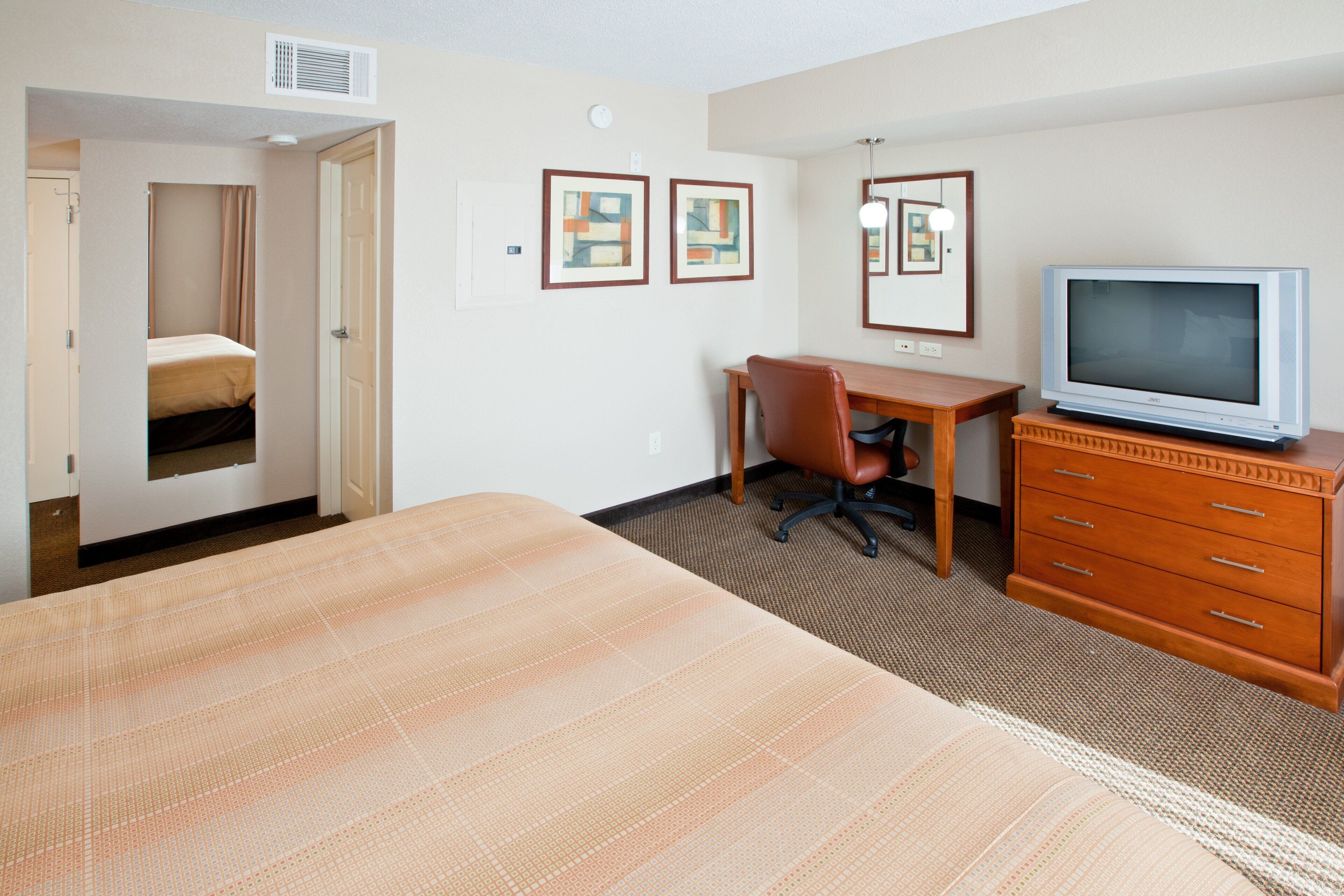 A hotel room with a bed, a desk, a chair, a television, and a dresser.