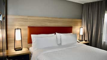 A hotel room with a bed, two bedside tables, a nightstand, a red headboard, and a window with curtains.