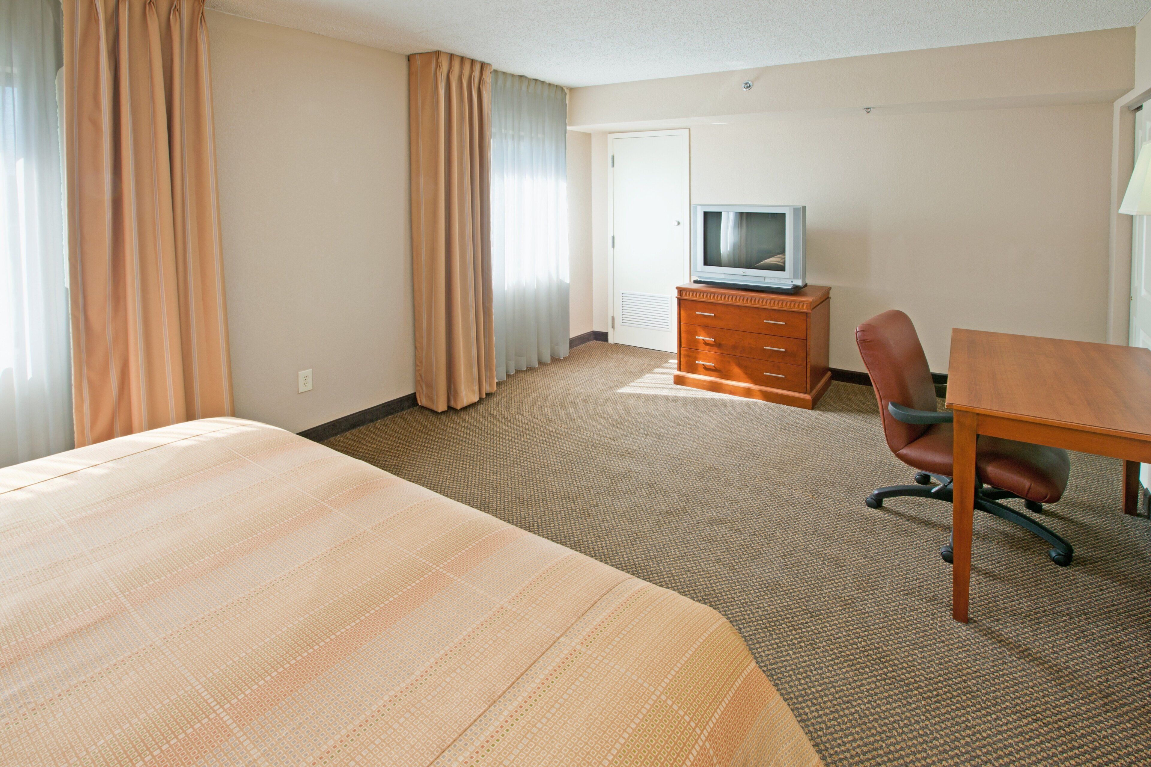A hotel room with a large bed, a wooden dresser, a television, and a desk.