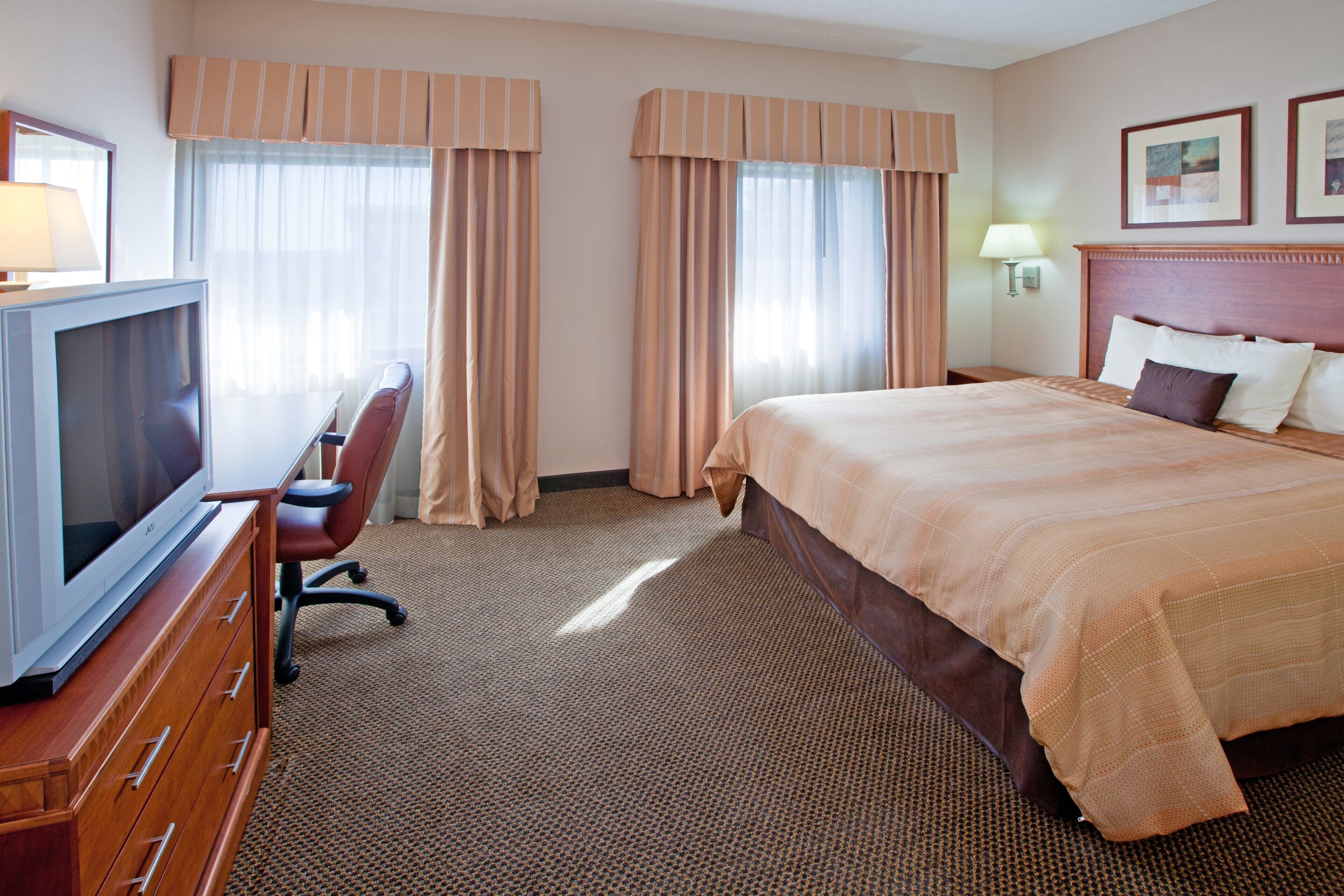 A hotel room with a bed, a desk with a television, and curtains.