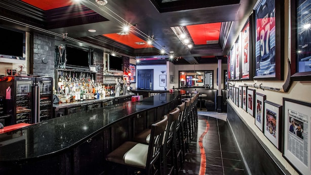 Una zona de bar con una barra larga, diversas opciones de asiento y una amplia variedad de botellas y vasos en estanterías.