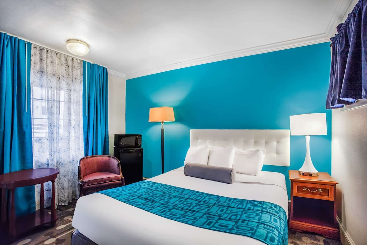 Ein Hotelzimmer mit einem großen Bett, einem Schreibtisch, einem Sessel, einem Fernseher und zwei Lampen.