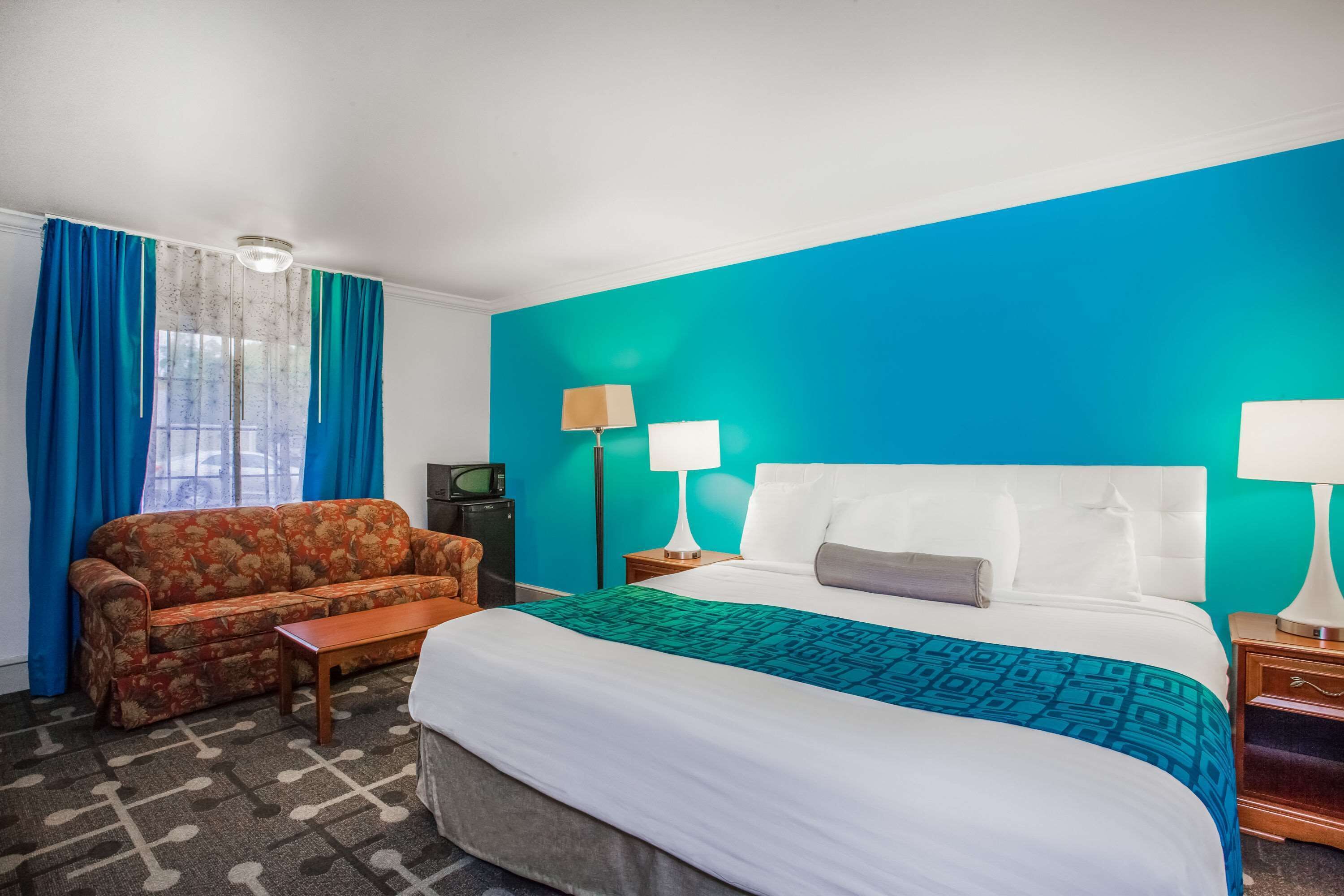 A hotel room with a bed, a sofa, a small table, and a nightstand with lamps.