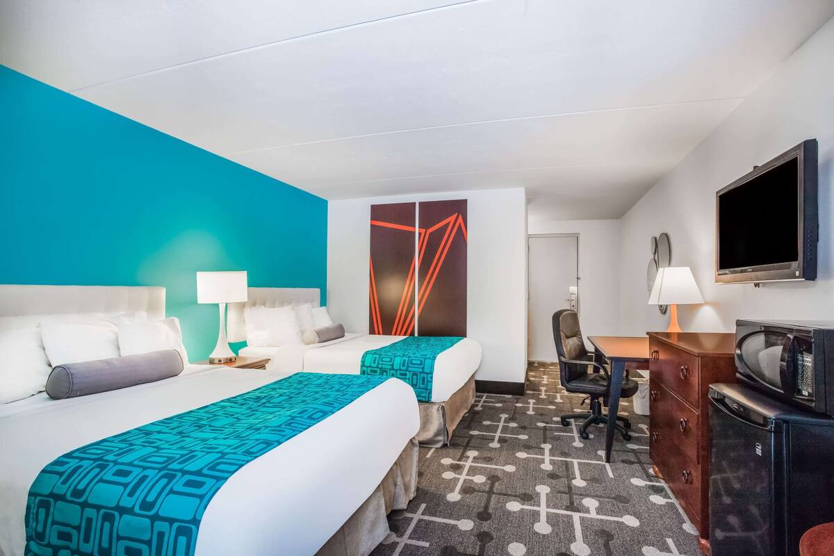 Ein Hotelzimmer mit zwei Betten, einem Schreibtisch, einem Stuhl, einem Fernseher und einer Mikrowelle.