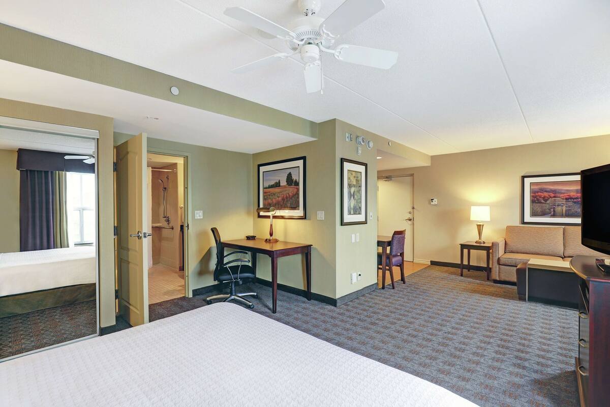 Une chambre d’hôtel équipée d’un lit, d’un bureau, d’une chaise, d’une télévision et d’un ventilateur de plafond.