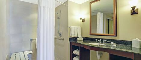 A hotel bathroom with a shower, a sink, a mirror, and shelves with towels.