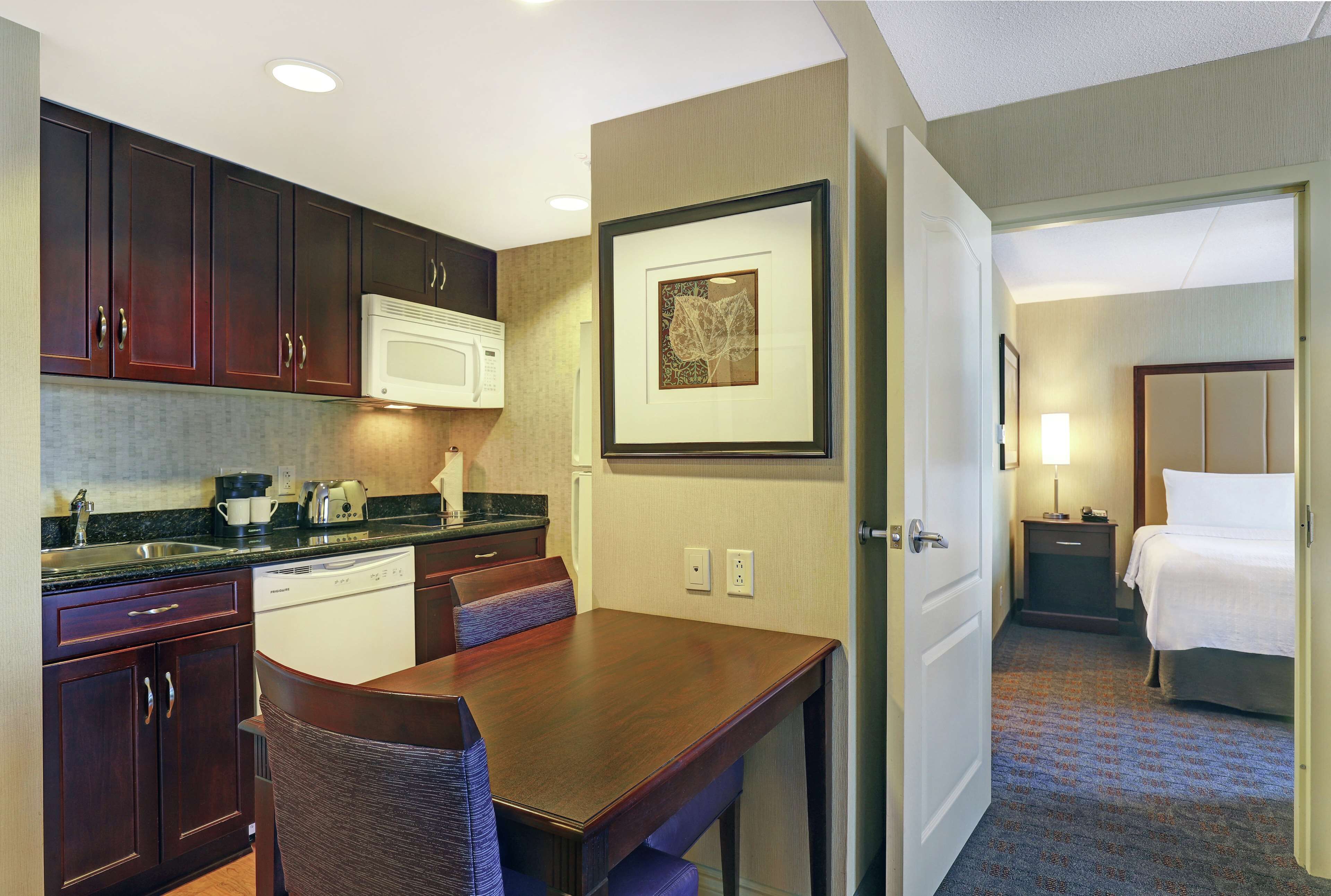 A hotel room with a kitchenette, a dining area, and a bed.