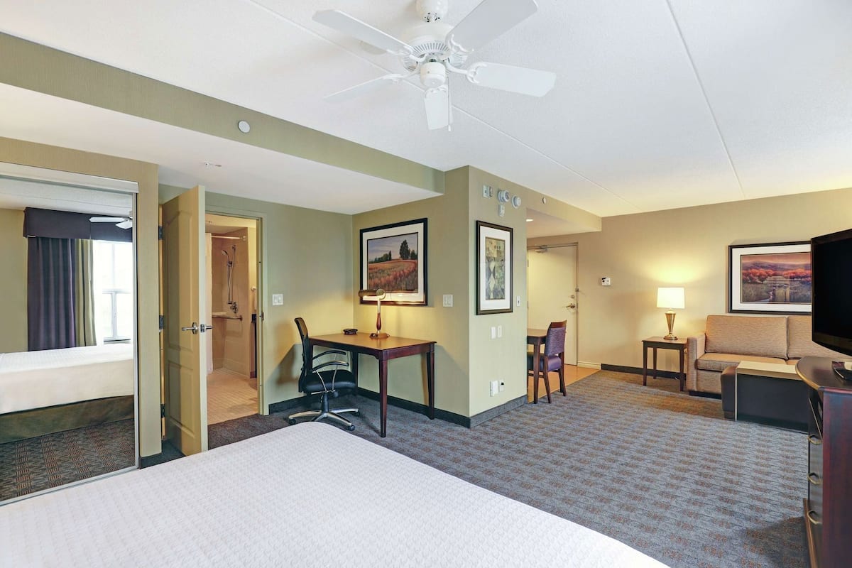 Habitación de hotel con cama, escritorio, silla, televisión y ventilador de techo.