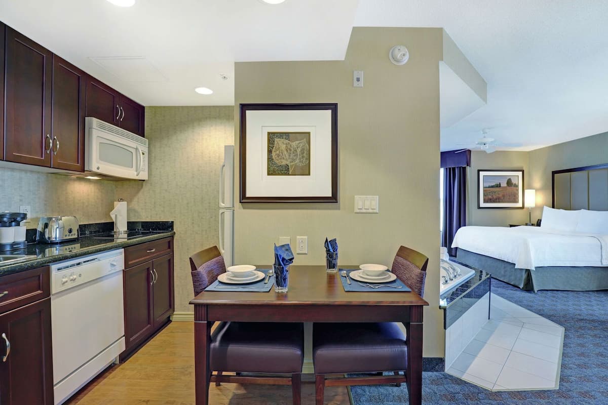 Habitación de hotel con kitchenette, mesa de comedor, sillas, cama y un cuadro en la pared.