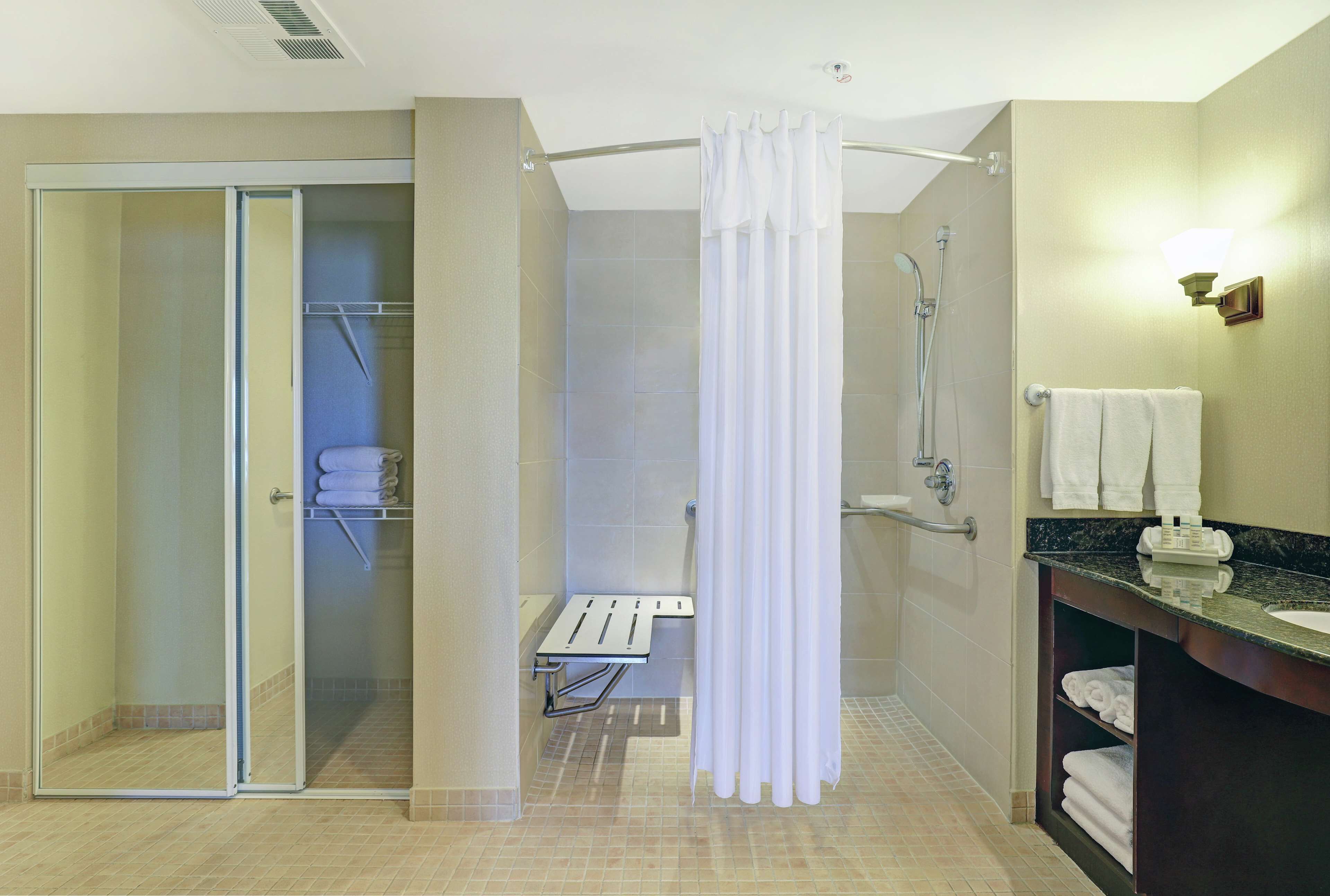 Un baño moderno con cabina de ducha de vidrio, cortina de ducha blanca, tocador con lavamanos y un perchero para toallas.