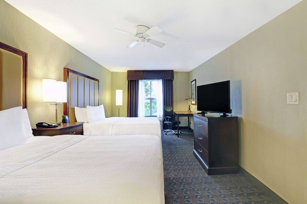 Une chambre d’hôtel avec deux lits, un bureau, une télévision et un ventilateur de plafond.