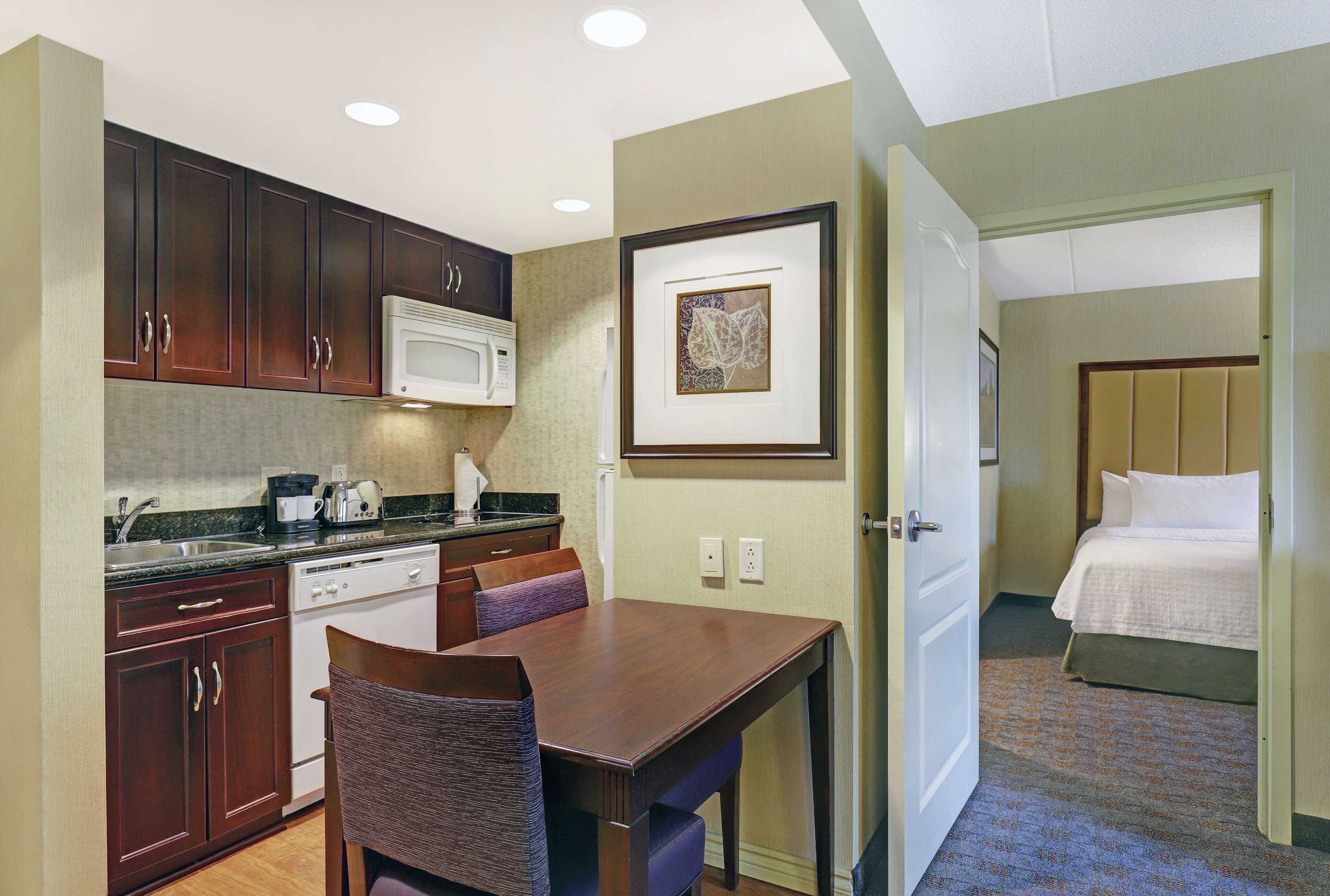 A compact hotel room with a kitchenette, a dining area, and a bed.