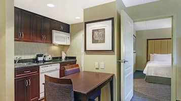 A compact hotel room with a kitchenette, a dining area, and a bed.