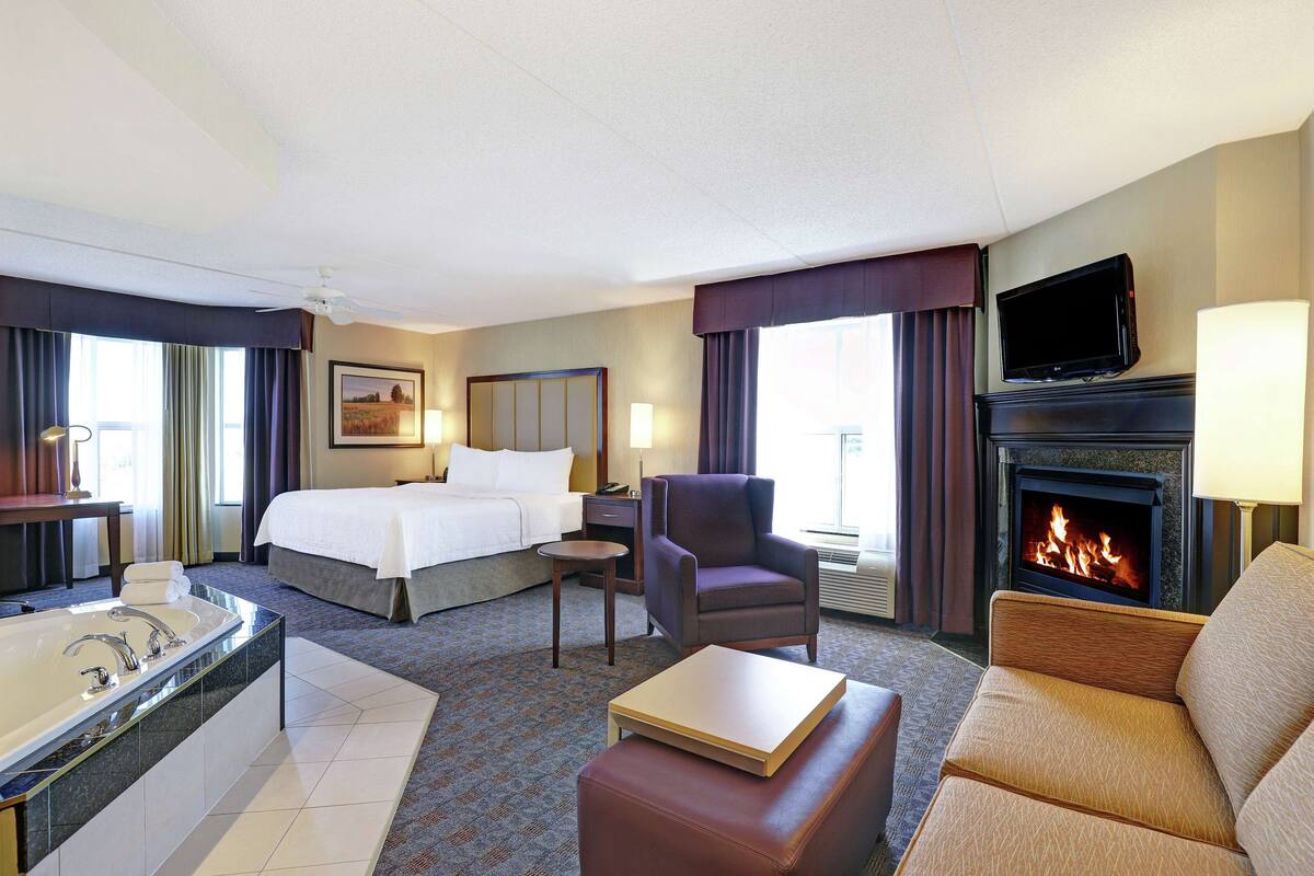 Une chambre d’hôtel comprenant un lit, un canapé, une télévision, une cheminée, une salle de bain avec baignoire et un bureau.