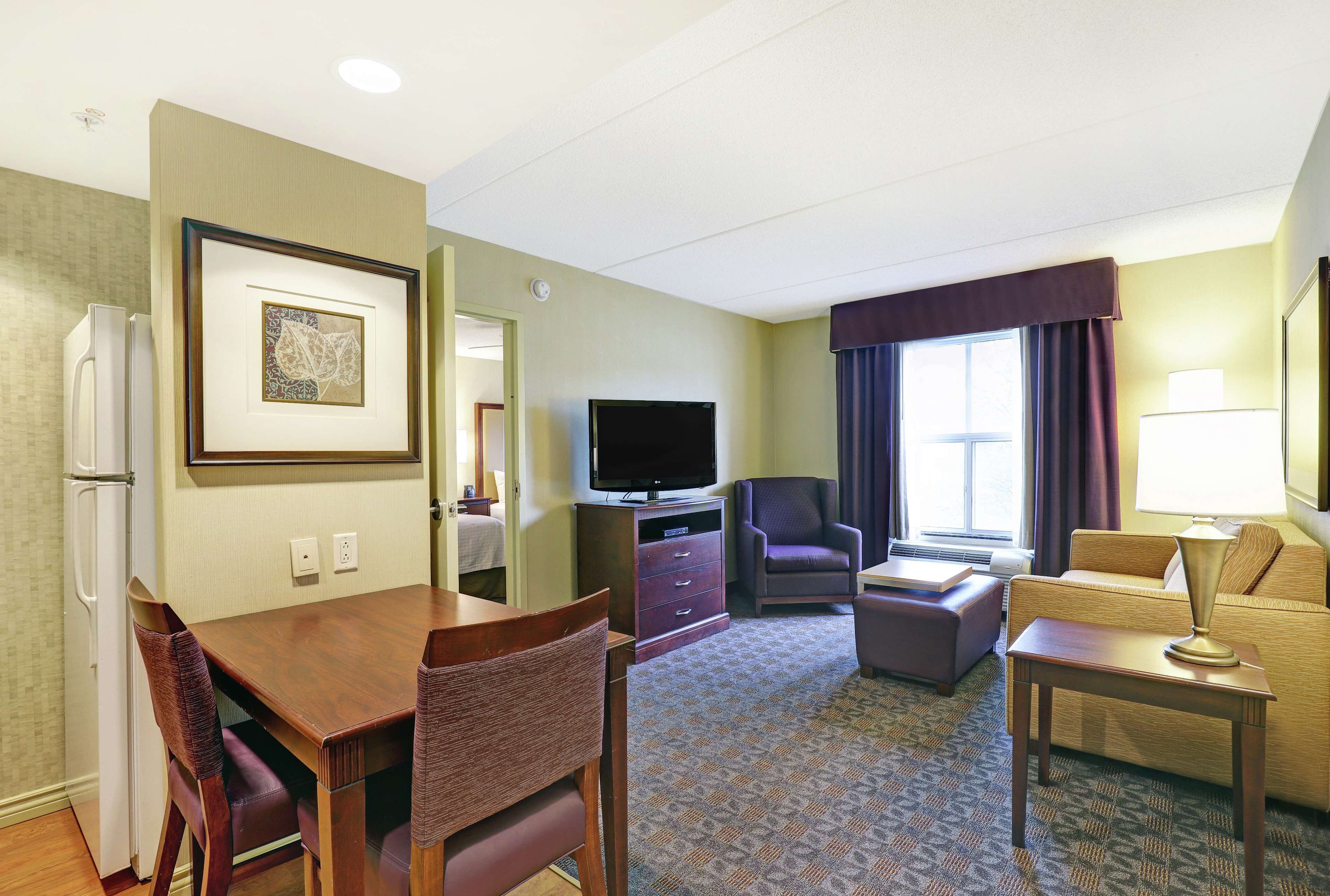 Una habitación de hotel con una mesa de comedor, sillas, televisión, sofá y una pequeña mesa con lámpara.