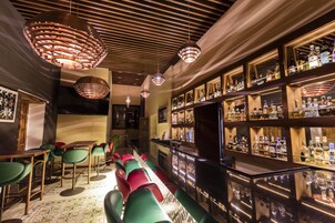 Zona de bar con diversas opciones de asientos, una amplia selección de licores y un diseño moderno en el techo.