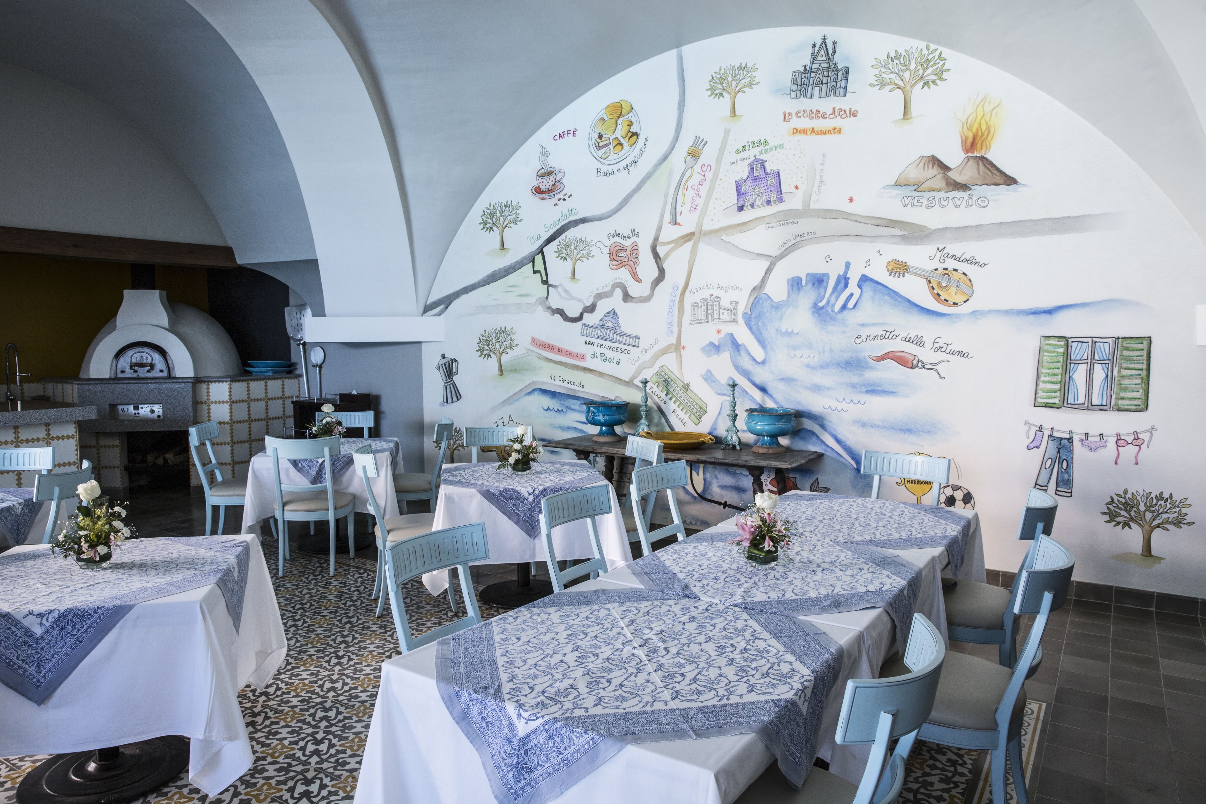 Ein Restaurant mit gedeckten Tischen, Wandgemälde und einem Pizzaofen im Hintergrund.