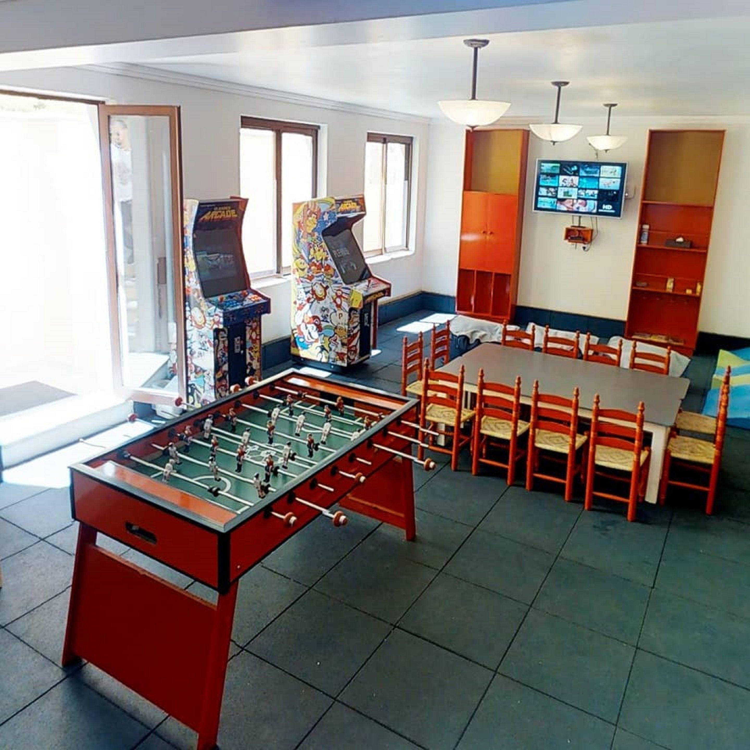 Una habitación con mesa de fútbolín, juegos de arcade, televisor y comedor con sillas y mesa.