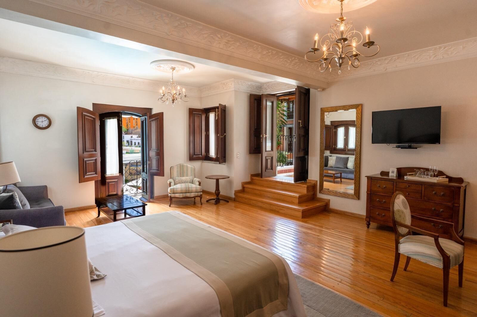 Habitación de hotel con cama, una silla, tocador, televisor y una escalera que lleva a un área exterior.