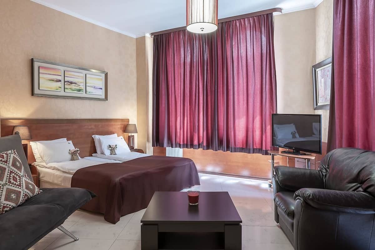 A hotel room with a bed, a sofa, a TV, and a table with a glass of water.