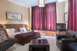 A hotel room with a bed, a sofa, a TV, and a table with a glass of water. - Maxim Boutique Hotel (Sofia)