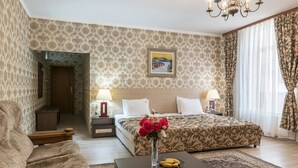 Habitación de hotel con cama, dos mesitas de noche, una mesita auxiliar, una mesa de centro con un jarrón de flores y un candelabro.