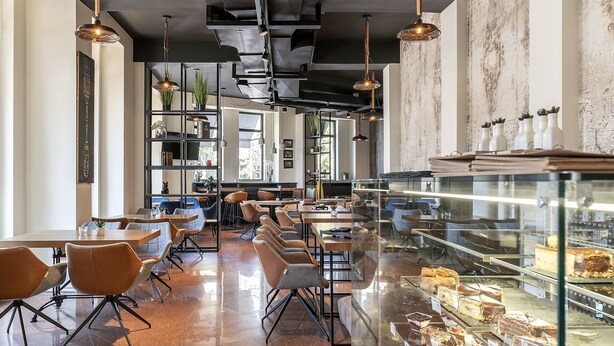 Una cafetería moderna con una vitrina de postres, mesas y sillas de madera.