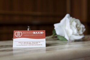 A hotel name card for Hotel Maxim with contact information and a white rose in the background. - Maxim Boutique Hotel (Sofia)