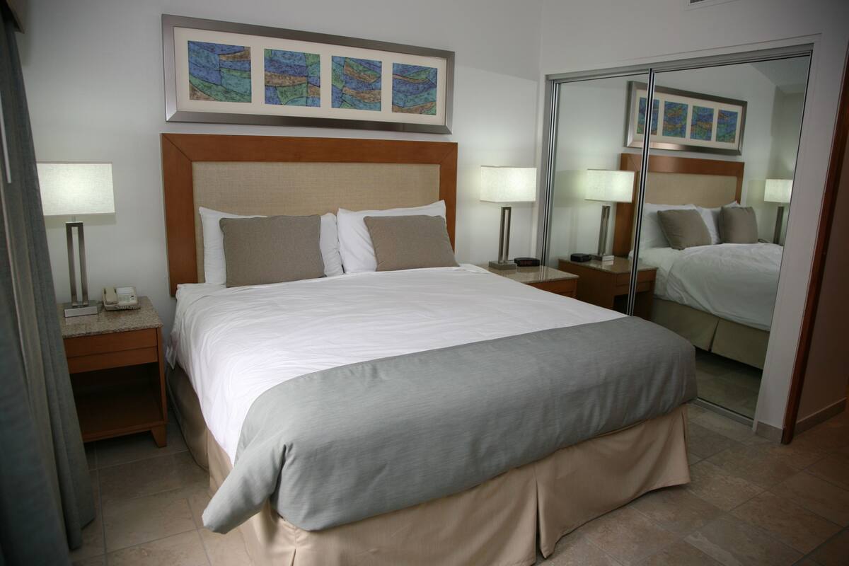 Une chambre d’hôtel avec un grand lit, deux tables de chevet avec des lampes, un miroir et des œuvres d’art accrochées au mur.