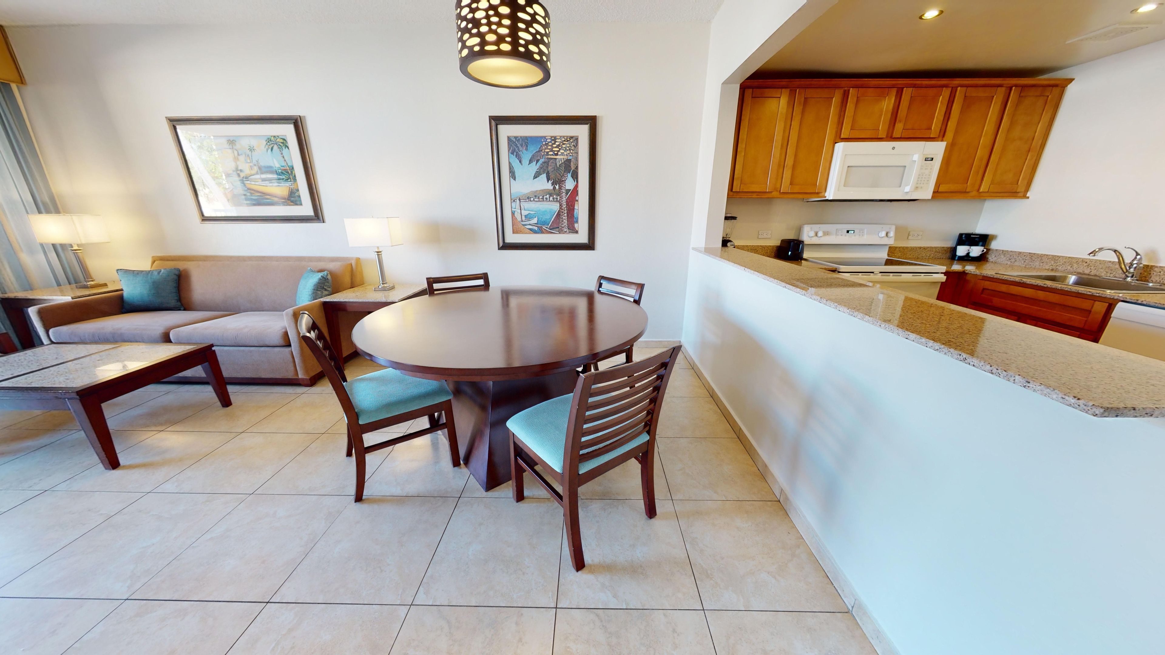 Una sala de estar moderna con una mesa de comedor redonda, dos sofás y una cocina con armarios de madera y un microondas.