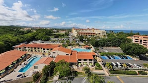 Un complexe hôtelier doté de plusieurs piscines, d’un grand bâtiment surmonté d’un toit recouvert de tuiles rouges et offrant une vue sur l’océan.