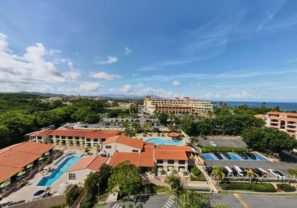 Ein Resort mit mehreren Schwimmbecken, einem großen Gebäude mit rotem Ziegeldach und Blick auf den Ozean.