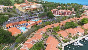 An aerial view of a coastal resort with multiple buildings, a marina, and a swimming pool.