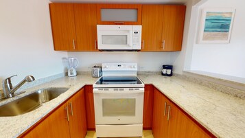 Cocina compacta con armarios de madera, microondas, tostadora, cafetera y horno empotrado.