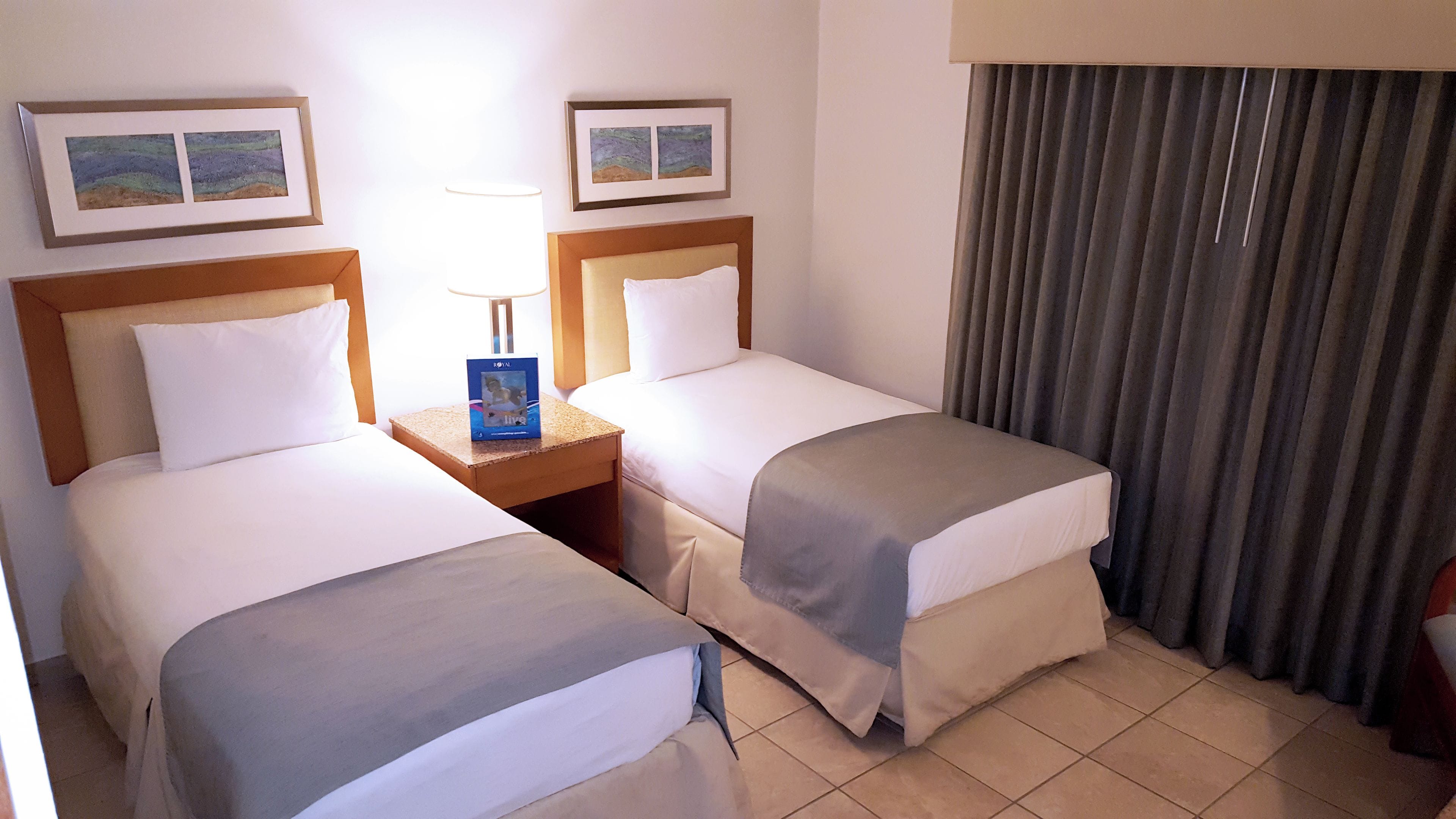 Habitación de hotel con dos camas, una mesita de noche, una lámpara y cortinas.