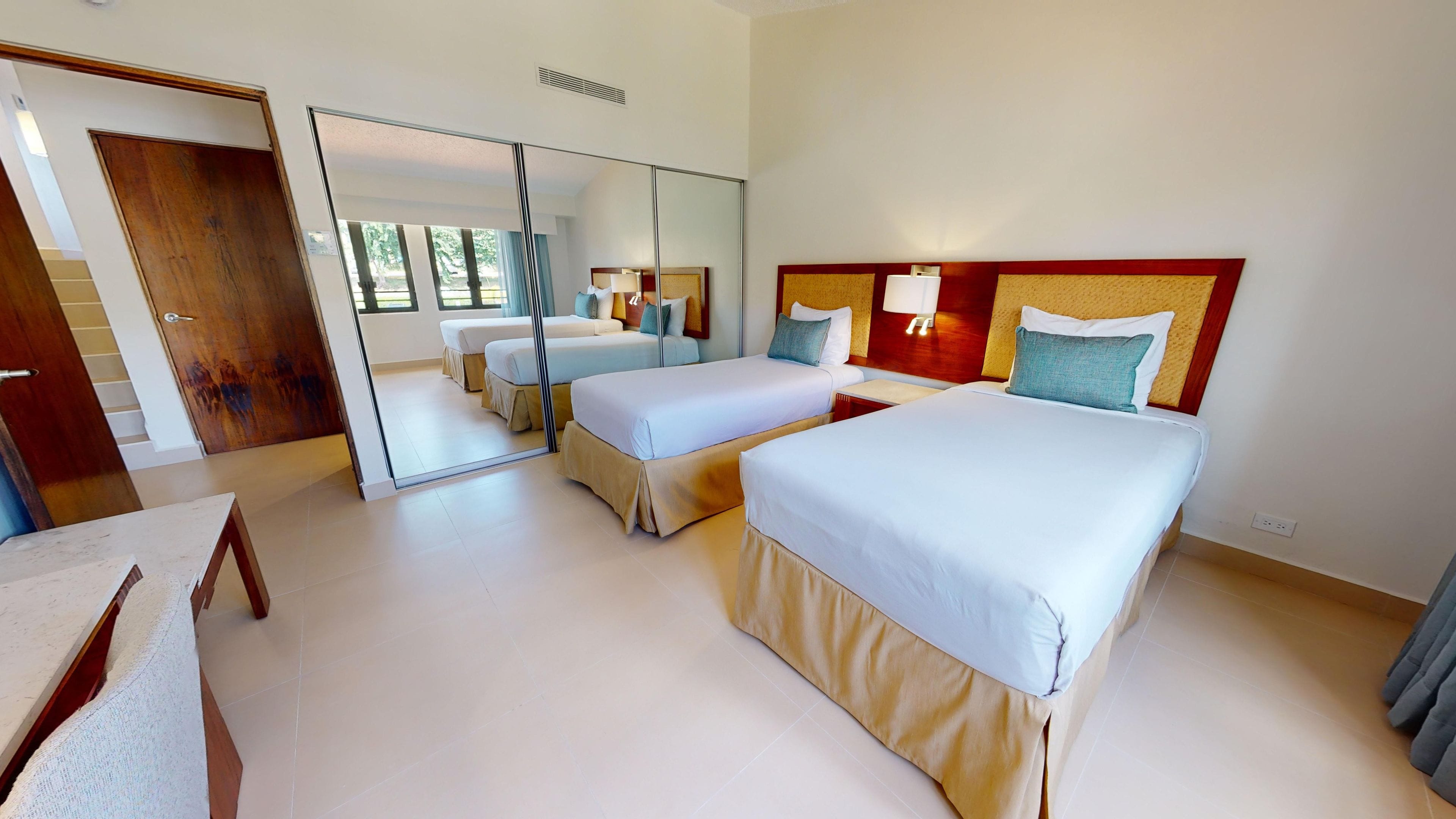 Habitación de hotel con dos camas, un espejo grande, una puerta de madera y vistas al exterior.