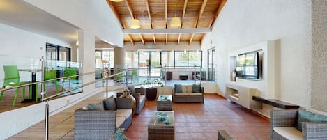 Un espacio interior amplio con mobiliario de mimbre, piscina y televisor en la pared.