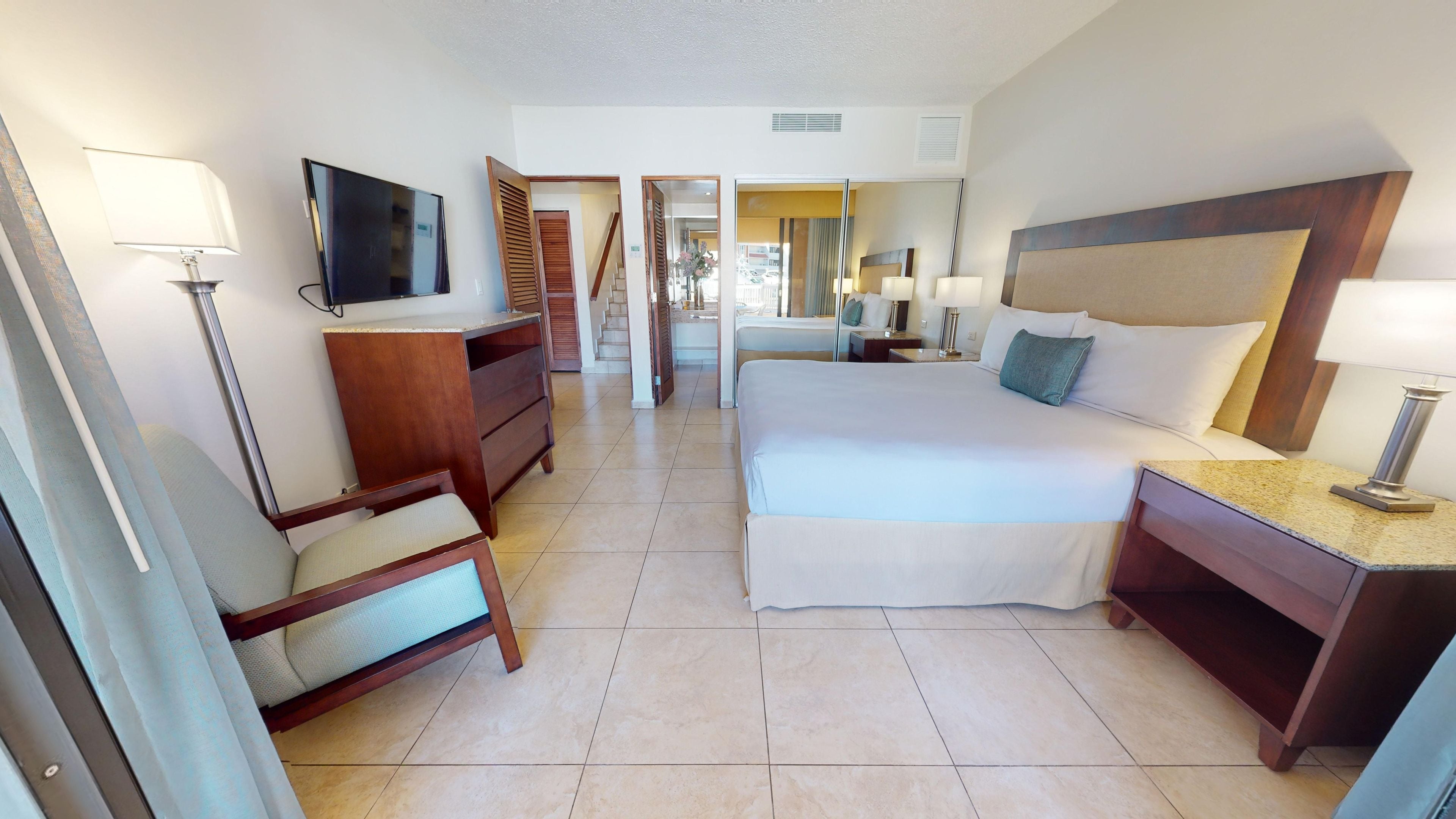 A hotel room with a bed, bedside tables, a TV, a desk, and a chair.