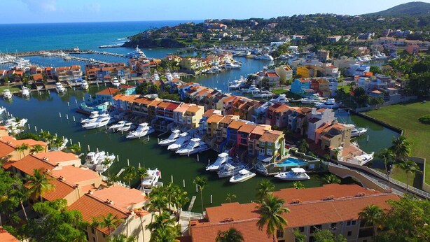 A marina with numerous boats docked, surrounded by colorful buildings with red-tiled roofs. - Park Royal Club Cala managed by Accor (Humacao)