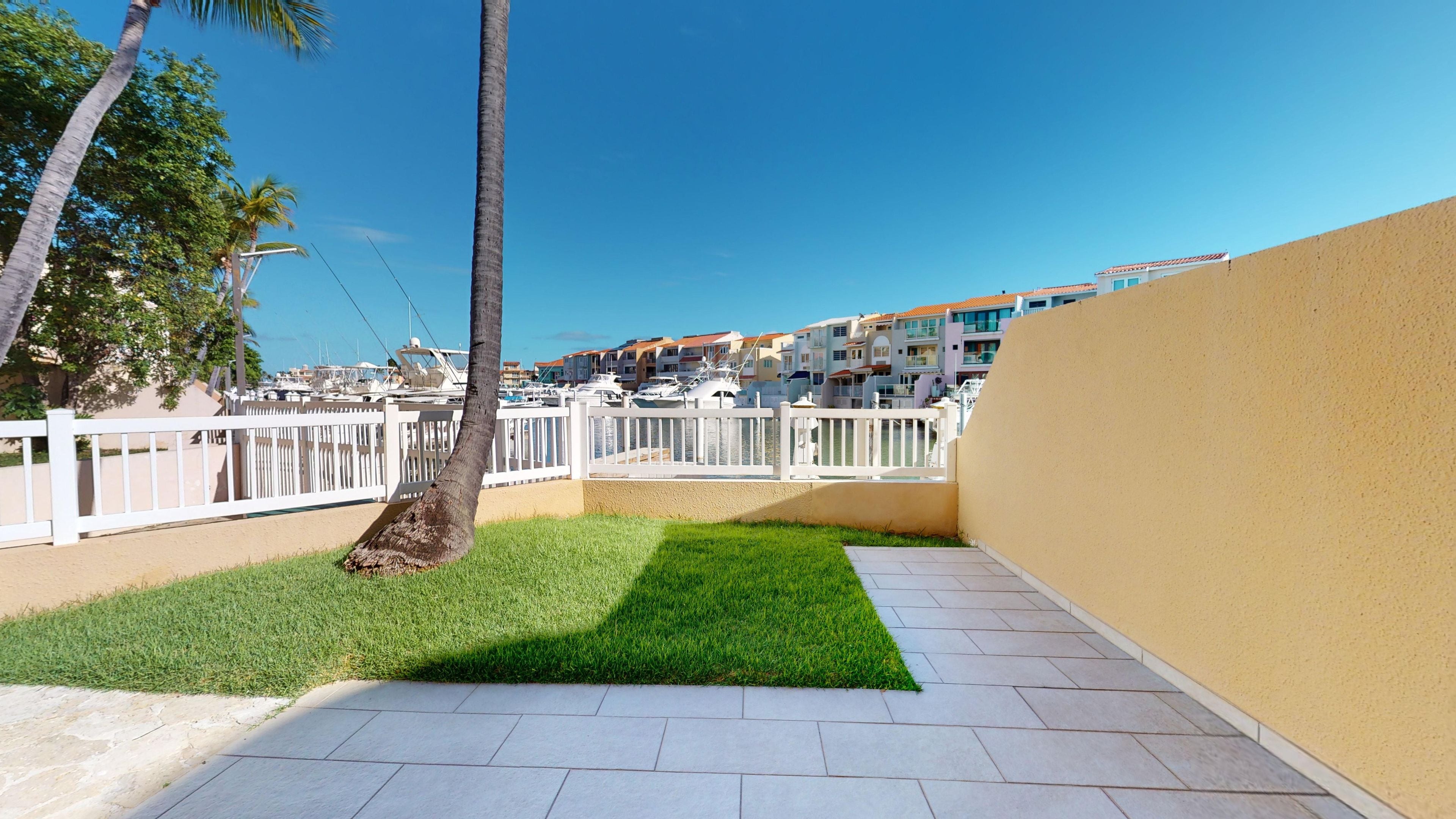 A paved patio area with a small lawn and a white fence.