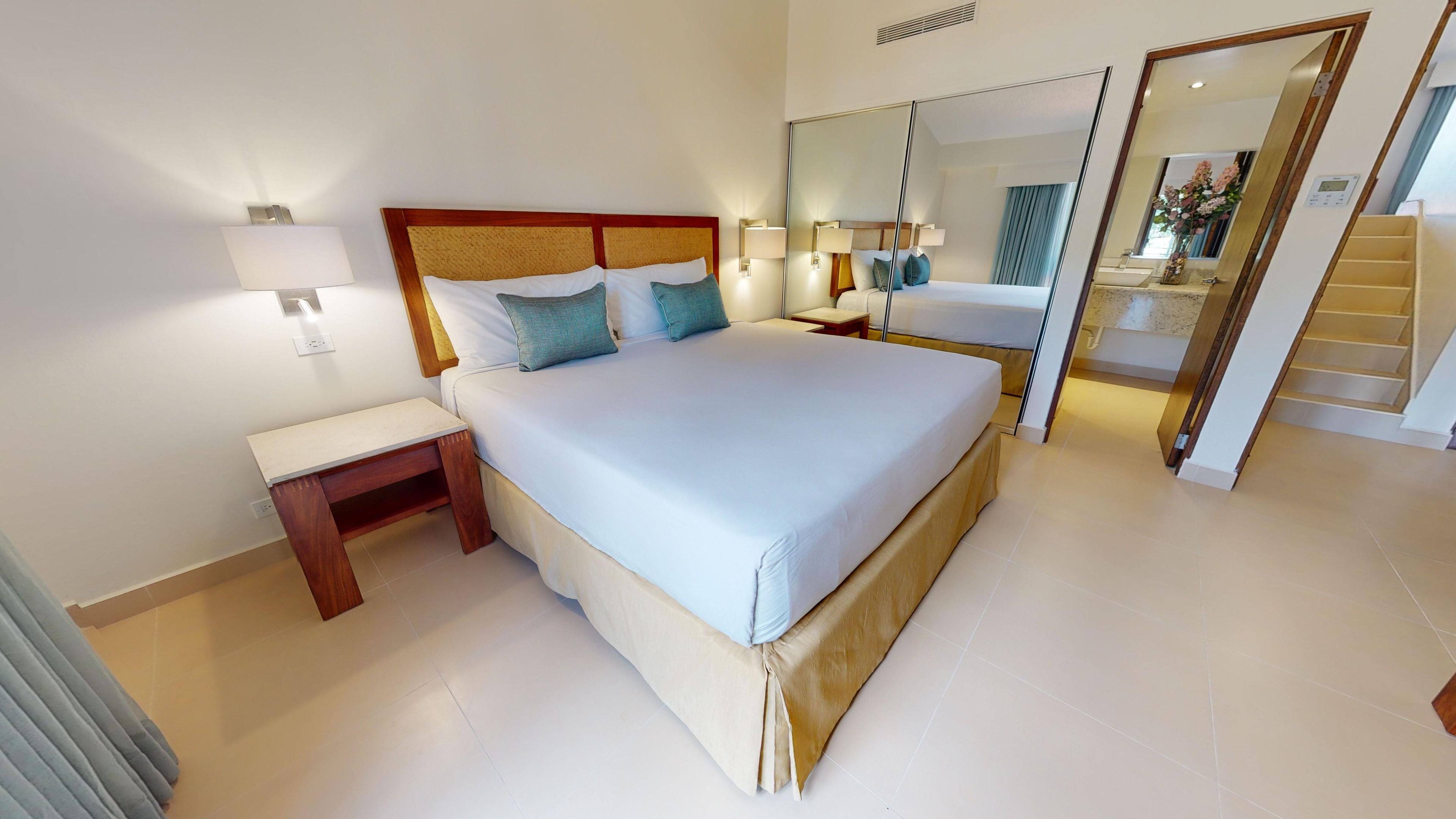 Una habitación de hotel con una cama grande, mesitas de noche, lámparas, un espejo y una escalera.