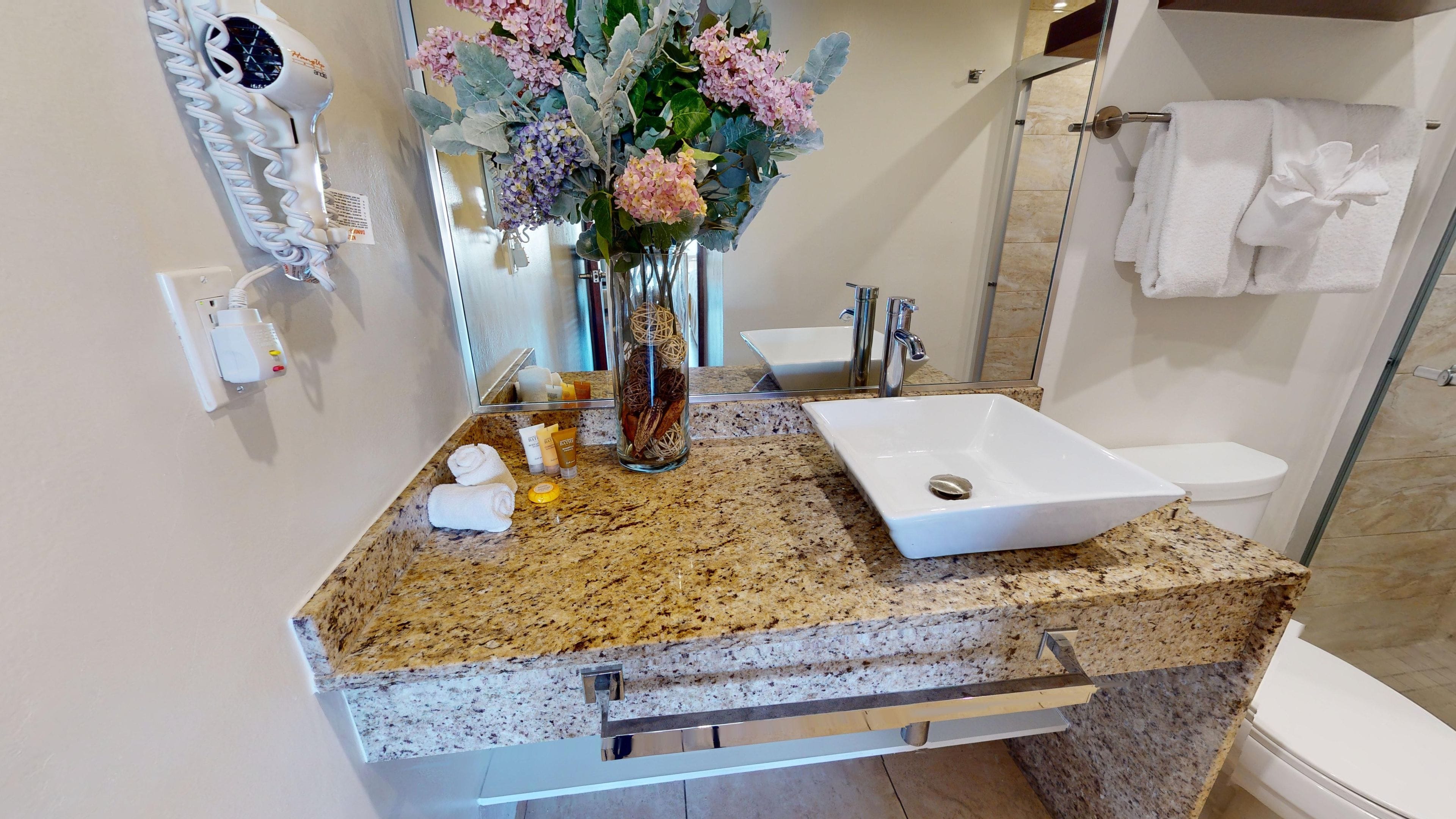 A bathroom with a granite countertop, a white sink, and a glass shower enclosure.