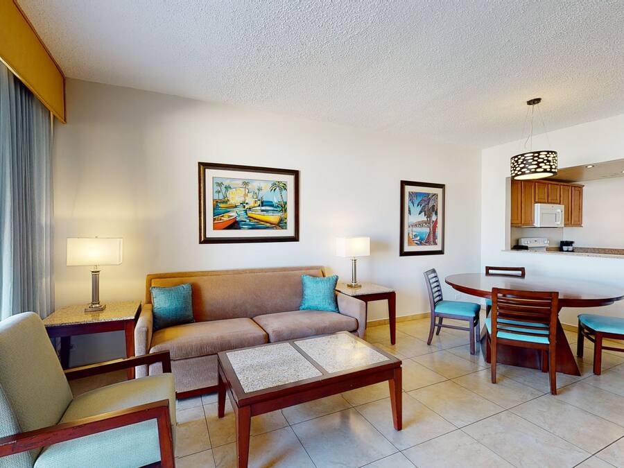 A hotel room with a sofa, chairs, a dining table, and artwork on the walls.