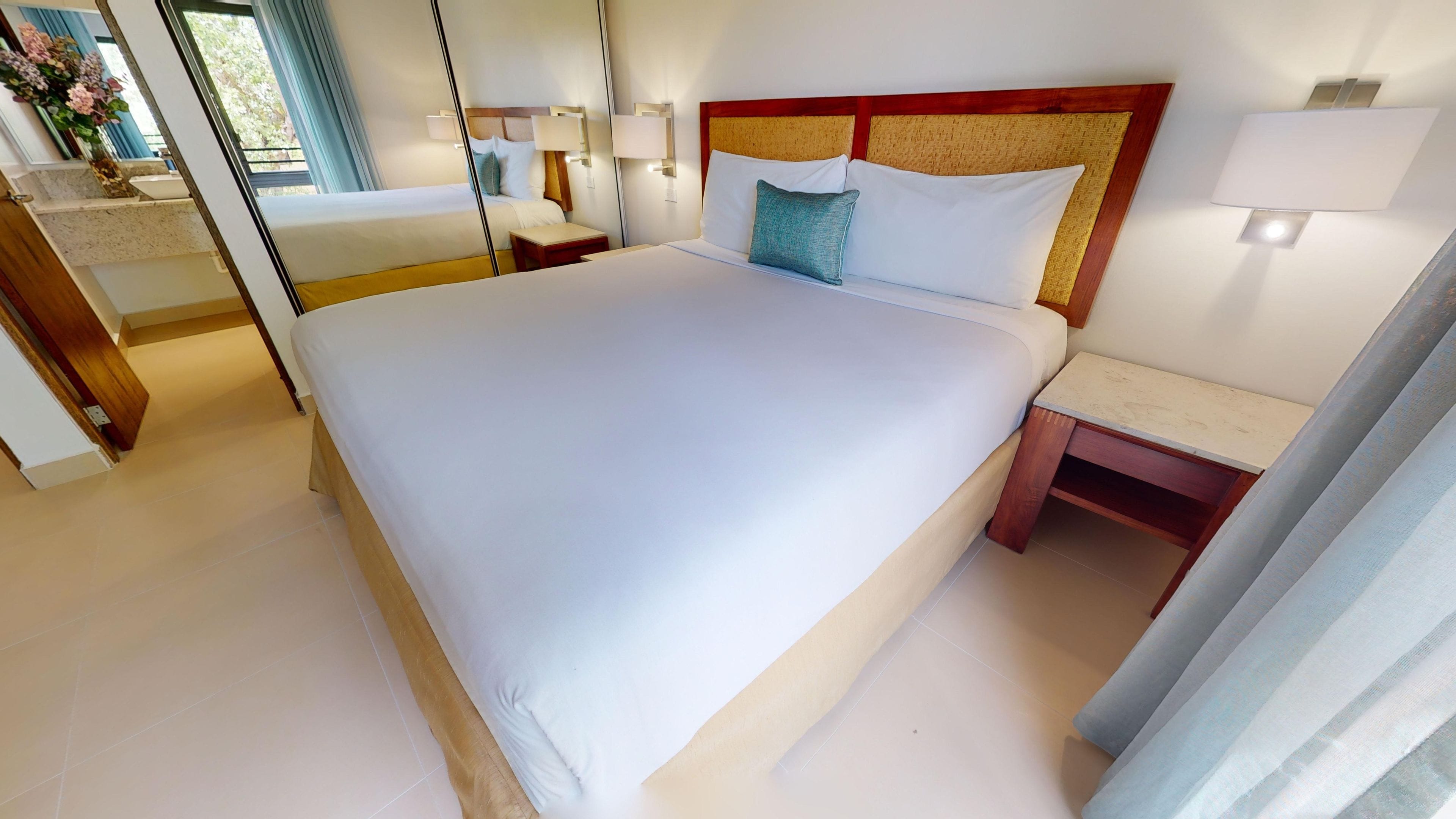 Quarto de hotel com uma cama grande, mesas de cabeceira e um espelho.