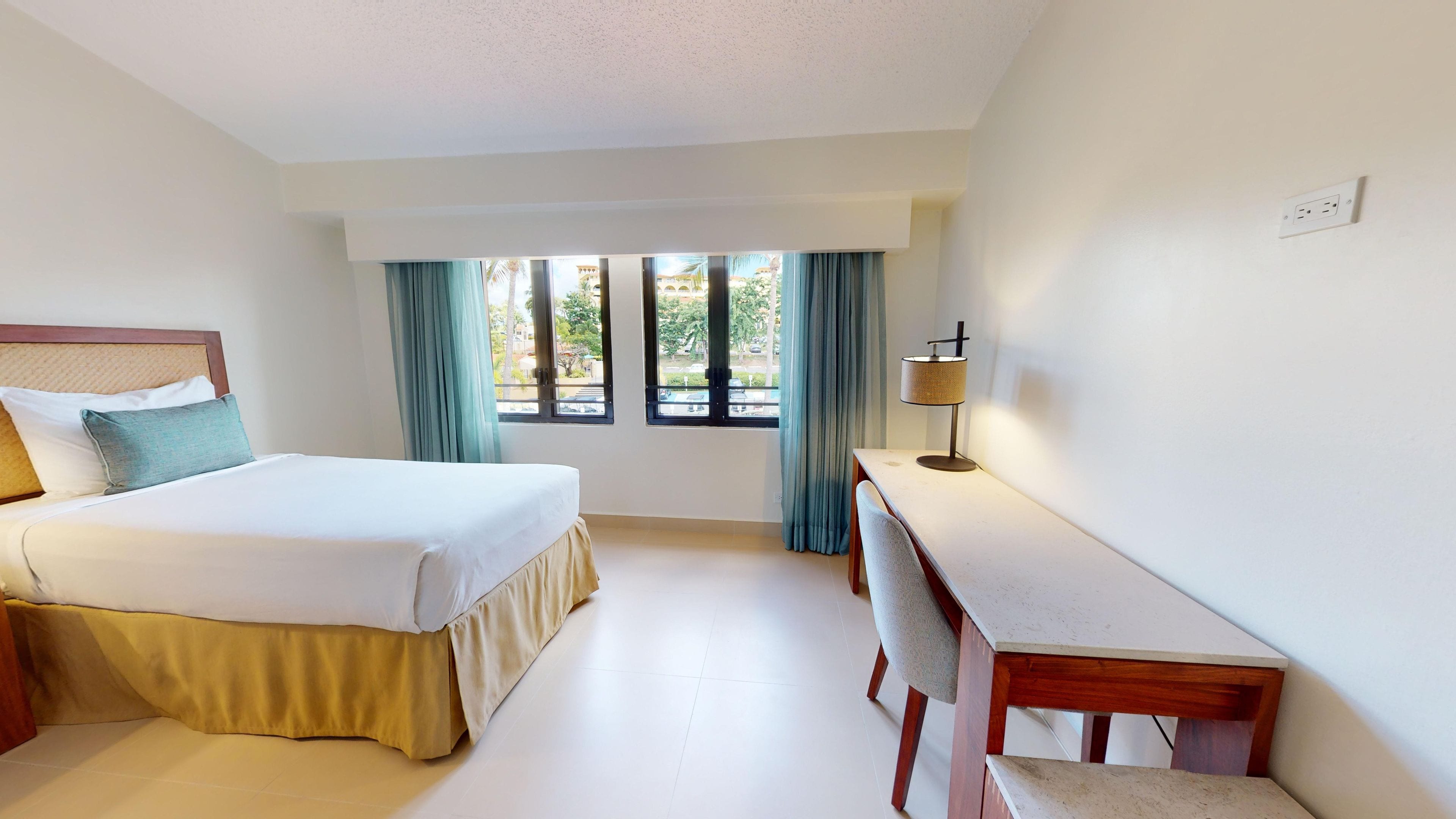 Een hotelkamer met een bed, bureau, lamp en raam met gordijnen.
